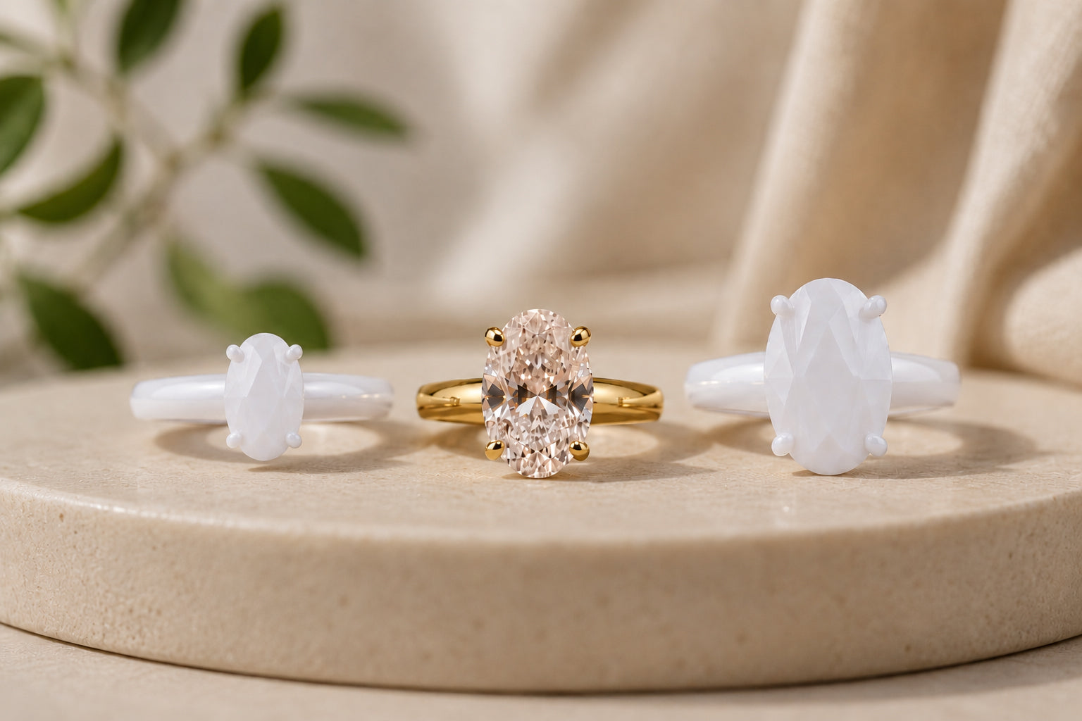 Three rings on display in 3 different size oval stones, the outer two in white printed material and the middles one in real gold and diamond material